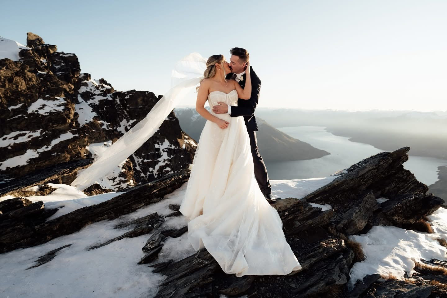 Couple in wedding attire standing on a snowy mountain landscape